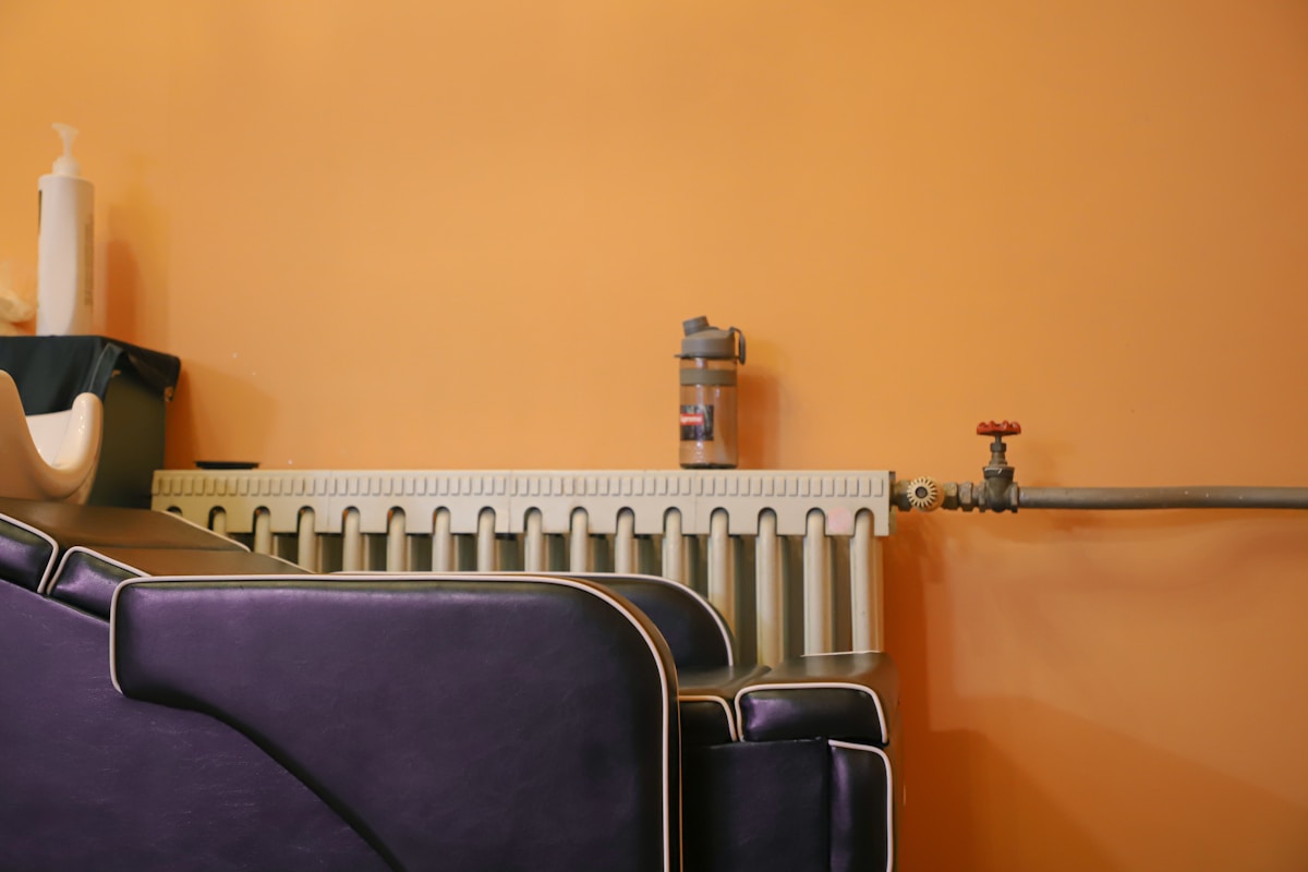 Radiateur, bouteille, robinet, mur orange, fauteuils violets.