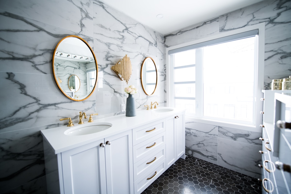 Salle de bain élégante avec carrelage marbré, miroirs dorés et mobilier blanc.