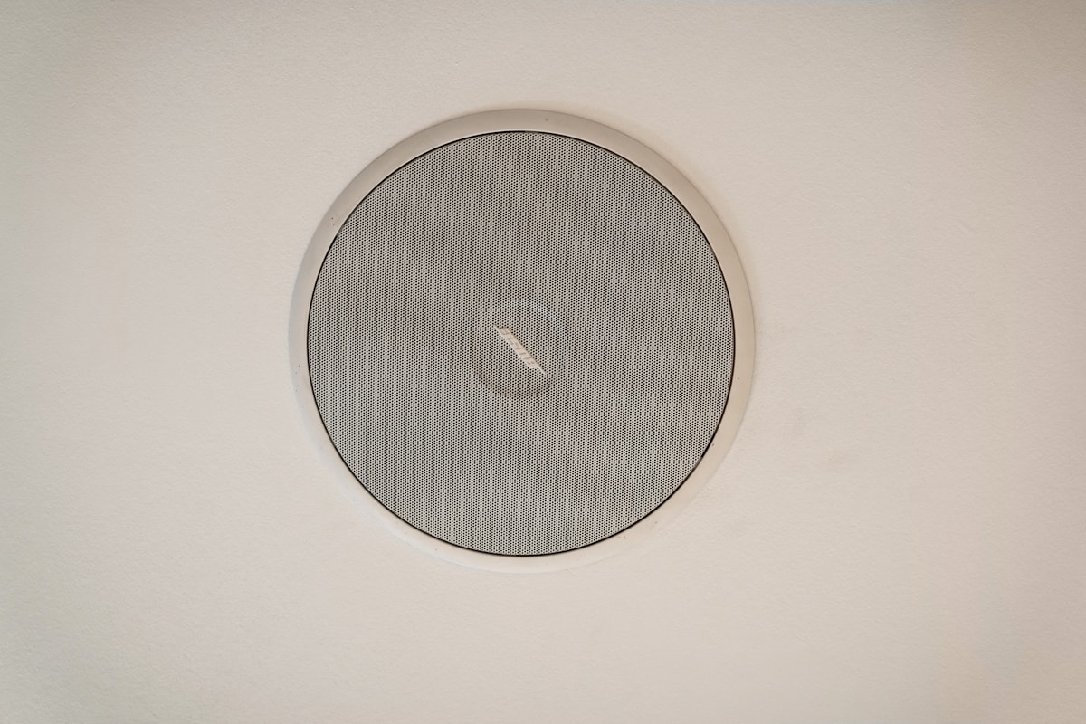 Haut-parleur rond encastré dans un mur blanc.