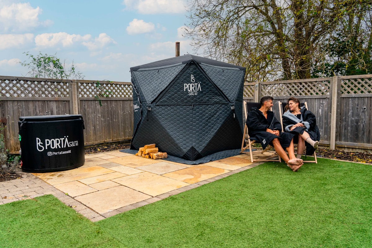 Abri portable noir avec logo, deux personnes assises sur des chaises, pelouse et pavés.