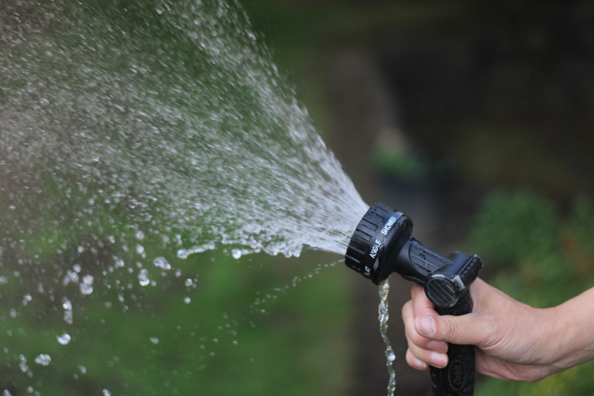 Jet d'eau puissant provenant d'un pistolet d'arrosage dans un jardin verdoyant.