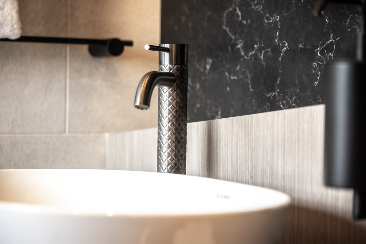 Robinet de salle de bain en métal texturé, évier blanc, mur de marbre noir.
