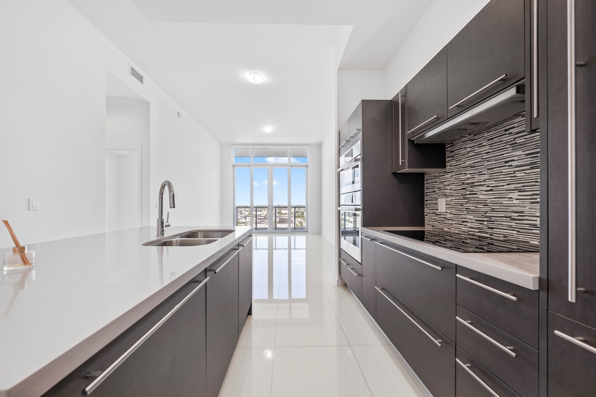 Cuisine moderne avec armoires noires, comptoirs blancs et fenêtre panoramique.