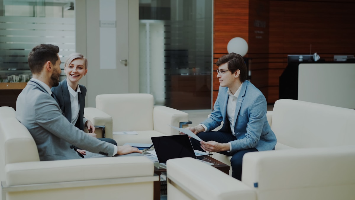 Trois personnes en costume d'affaires discutant autour d'un ordinateur portable dans un bureau moderne.