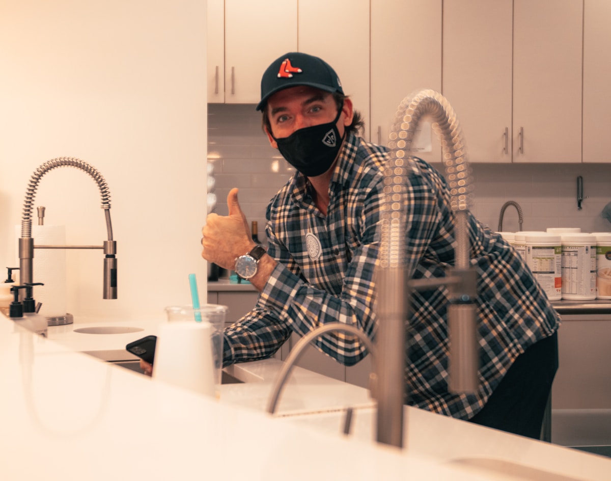 Homme avec casquette et masque dans une cuisine, donnant un pouce levé.