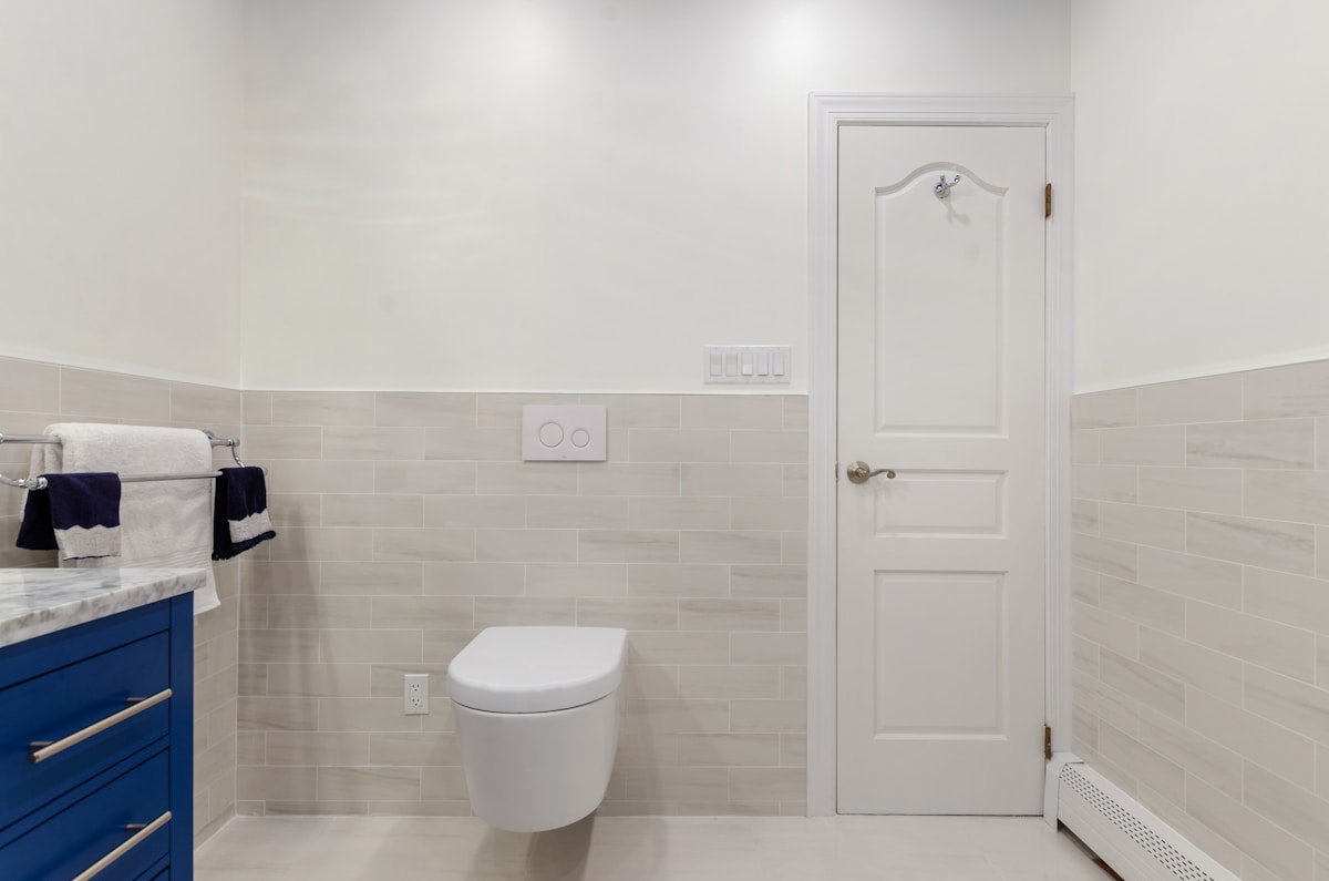 Salle de bain moderne avec carrelage gris clair, meuble bleu et porte blanche.