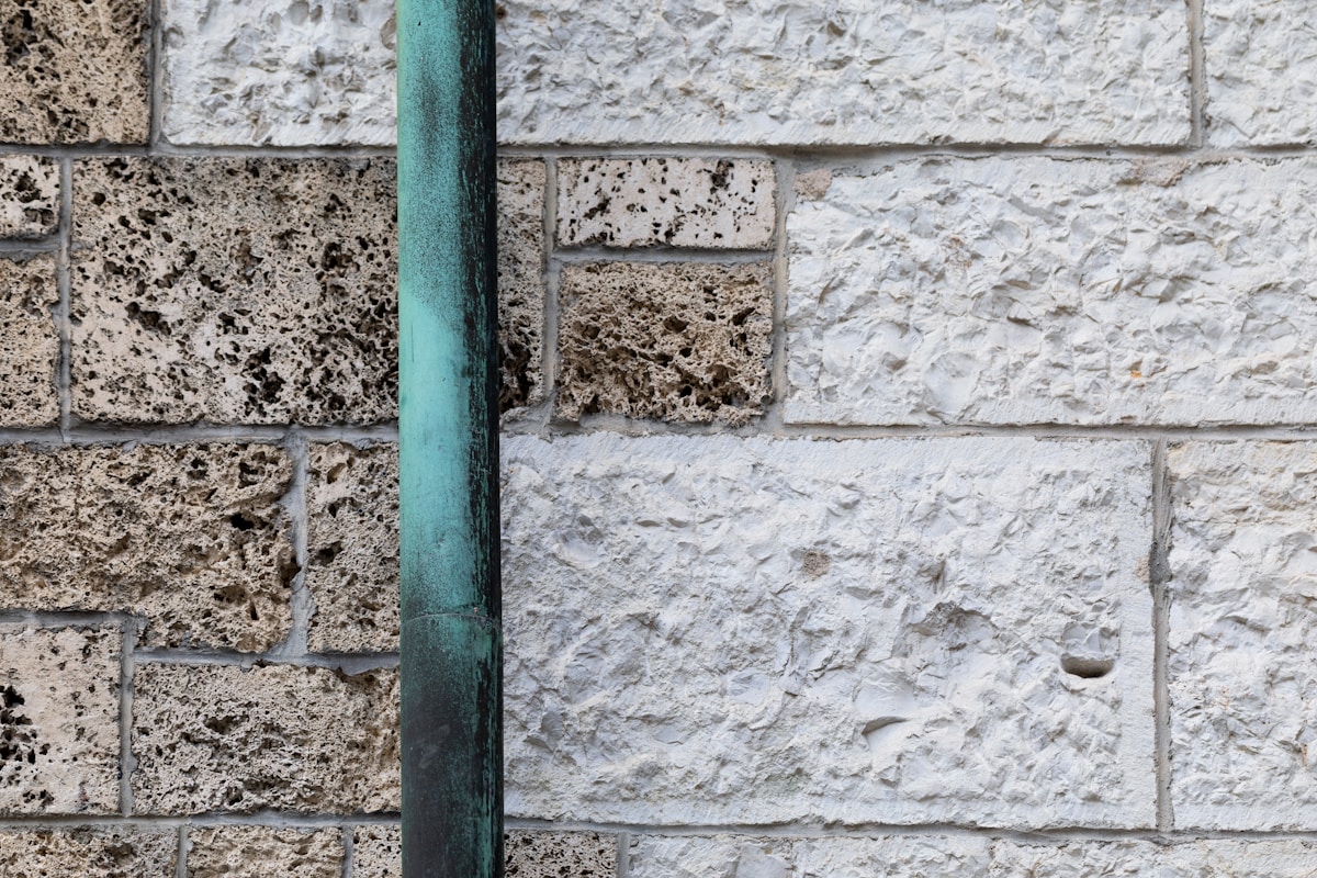 Mur de briques gris et tuyau vert vertical.