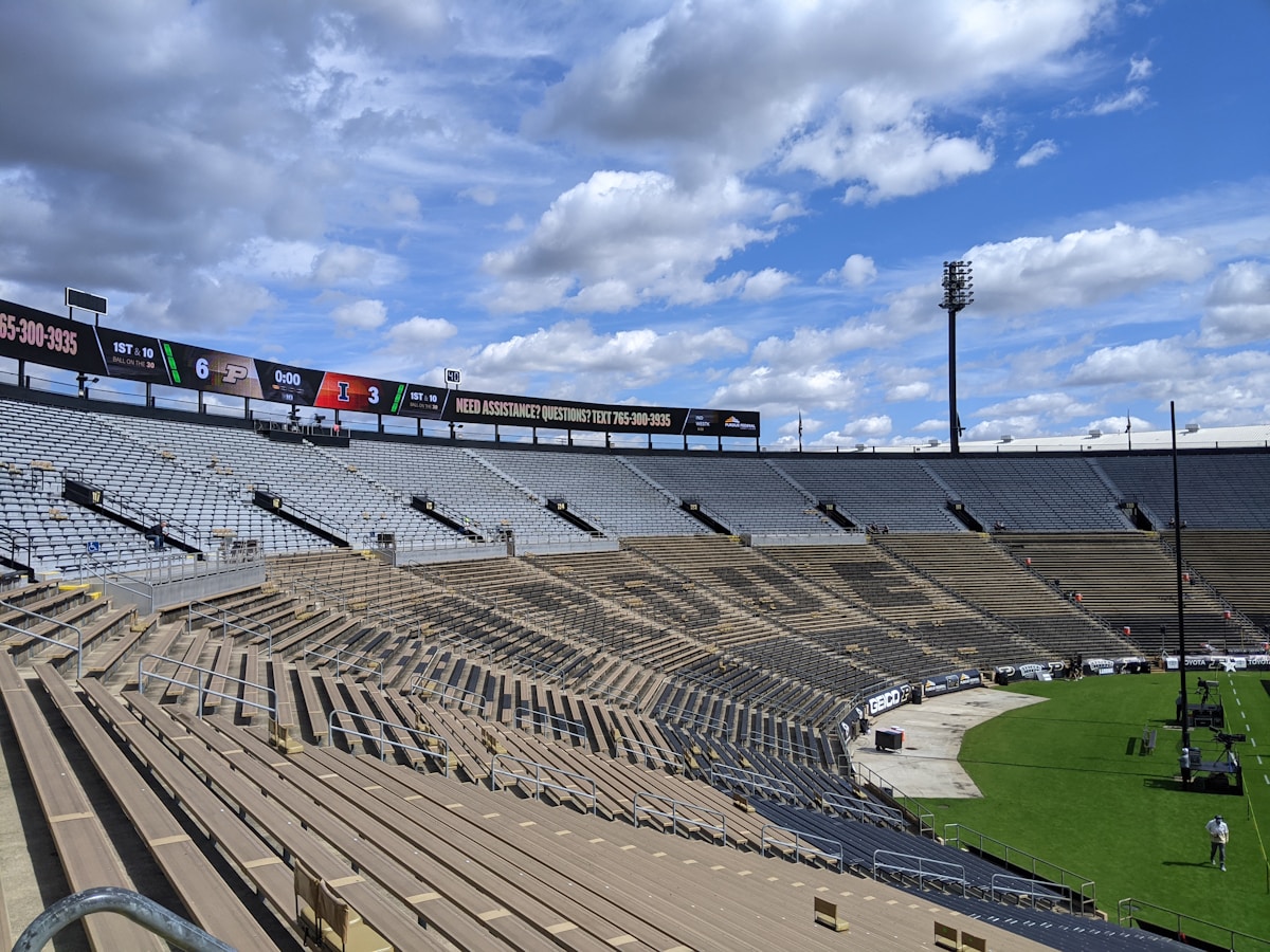Stade de football avec gradins vides, ciel nuageux et tableau d'affichage.