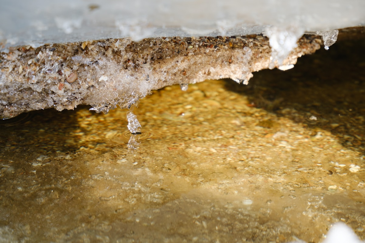 Rocher enneigé surplombant une eau dorée et cristalline.