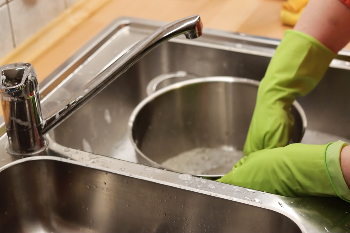 Évier de cuisine en acier inoxydable avec robinet et gant de ménage vert.