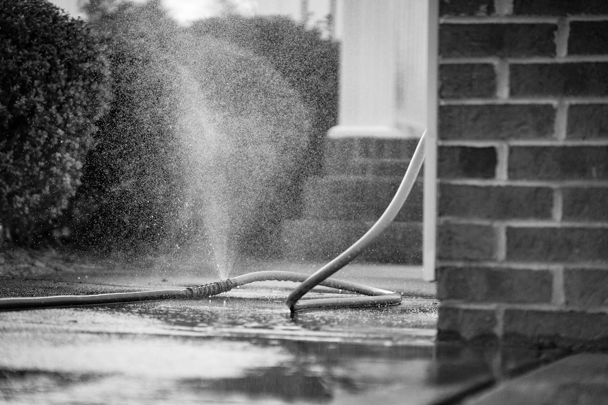 Jet d'eau puissant arrosant le sol mouillé près d'un mur de briques.