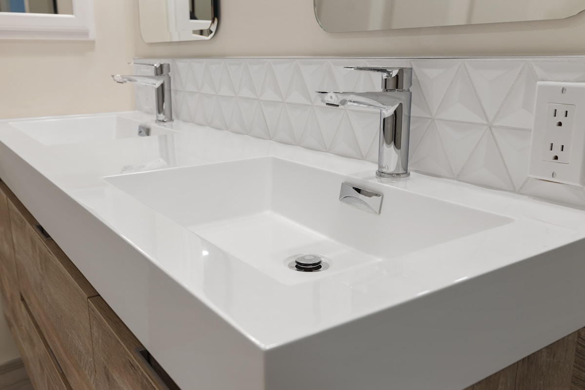 Lavabo blanc moderne avec robinet chromé et carrelage géométrique.