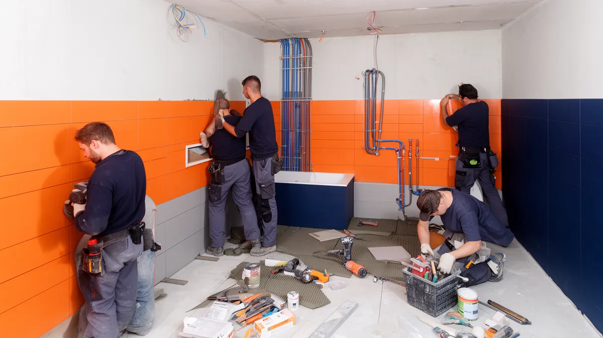 Plusieurs ouvriers rénovant une salle de bain avec des murs orange.