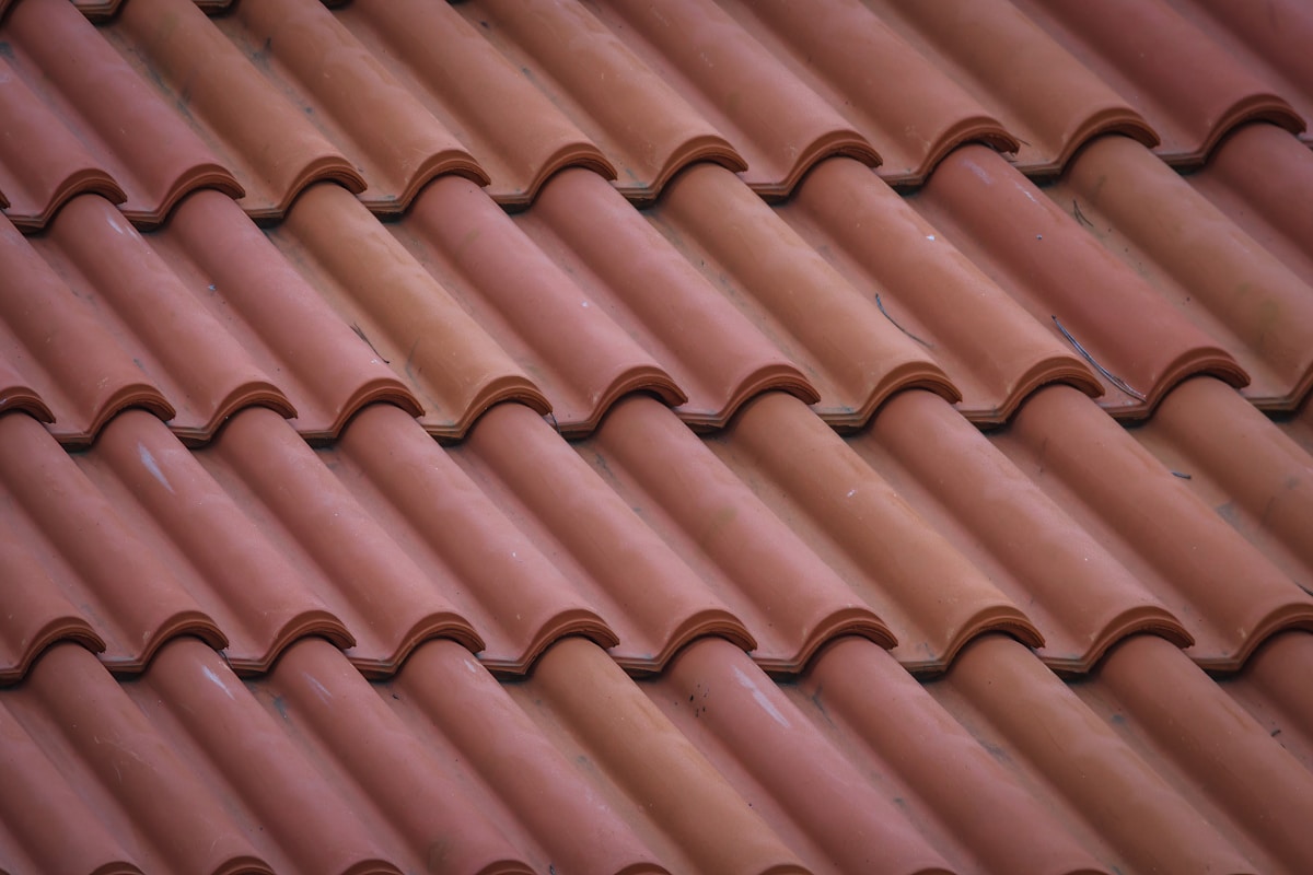Tuiles de toiture en céramique rouge ondulées alignées en rangées.