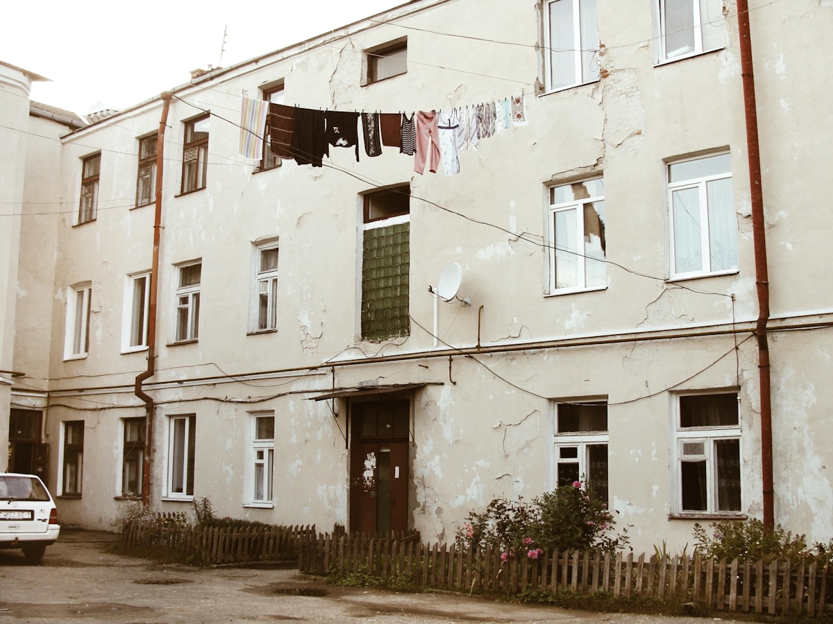 Bâtiment délabré avec linge suspendu, clôture en bois et végétation.
