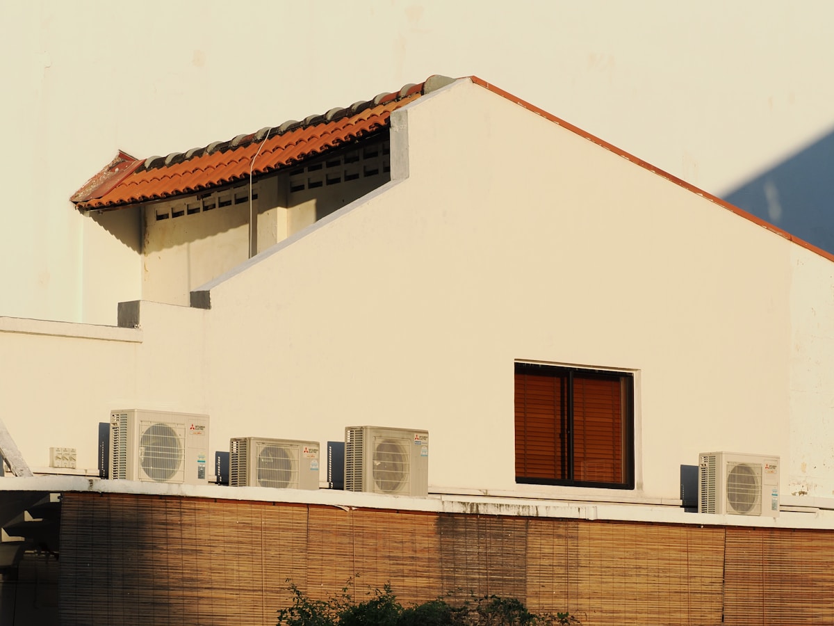 Bâtiment avec toit en tuiles rouges, murs blancs et unités de climatisation.