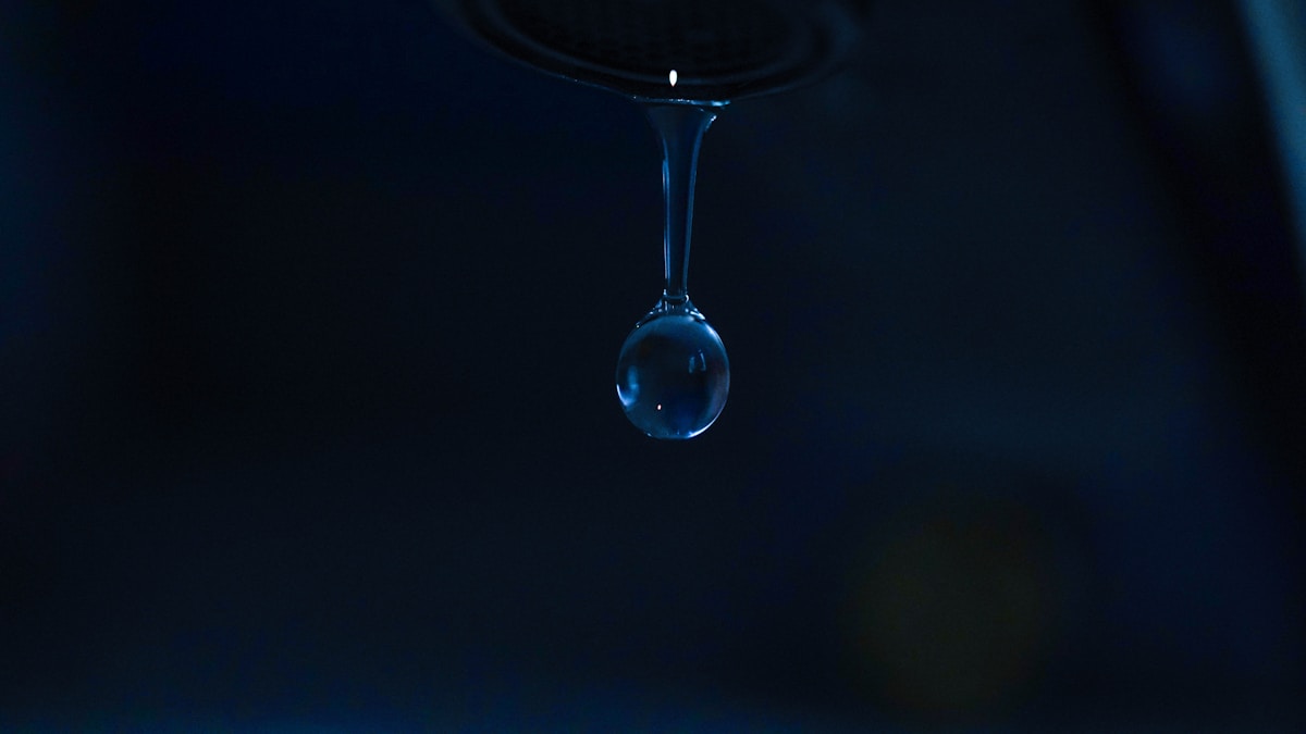 Goutte d'eau suspendue dans l'obscurité, reflet lumineux.