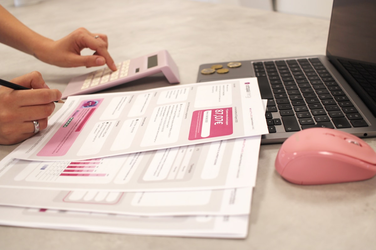 Calculs financiers, documents, ordinateur portable et souris rose sur un bureau.