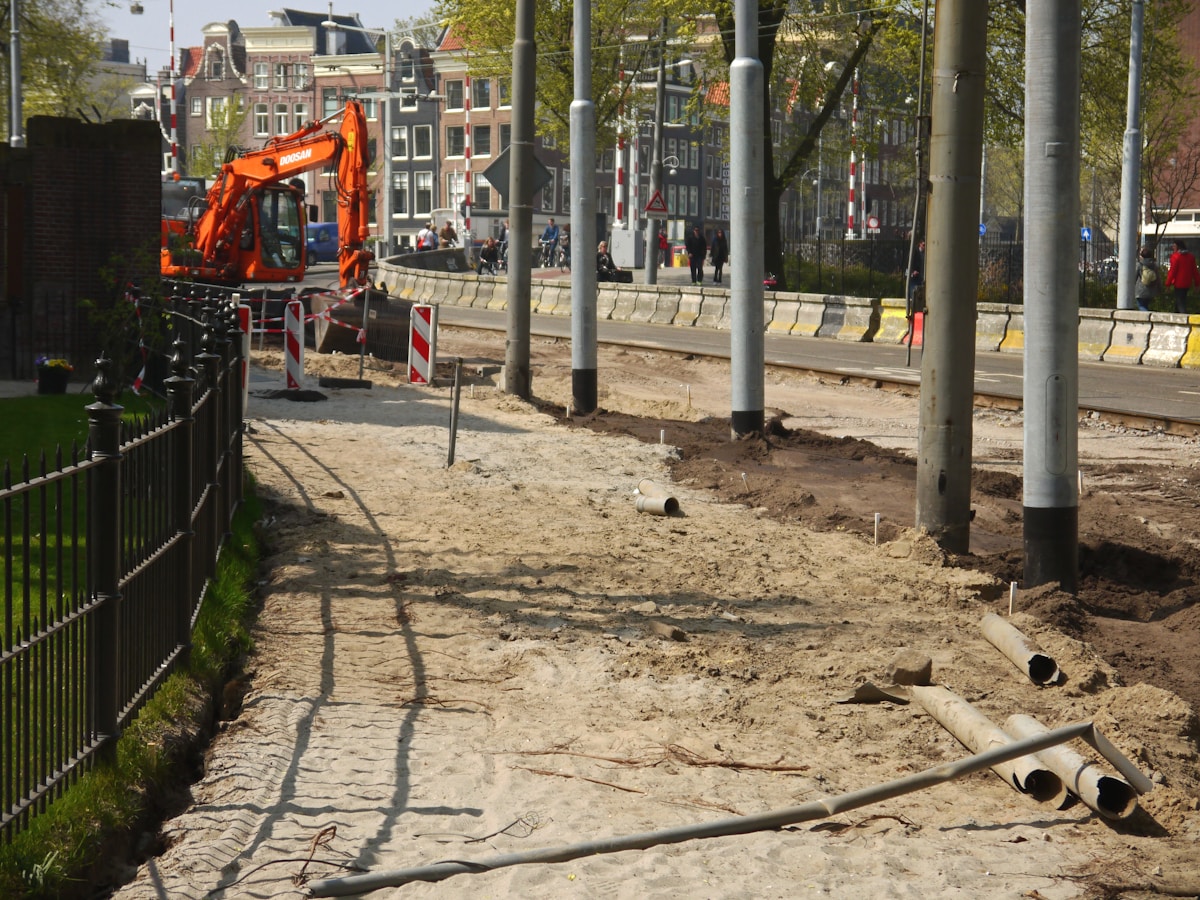 Chantier de construction urbain avec pelleteuse orange et trottoir en réparation.