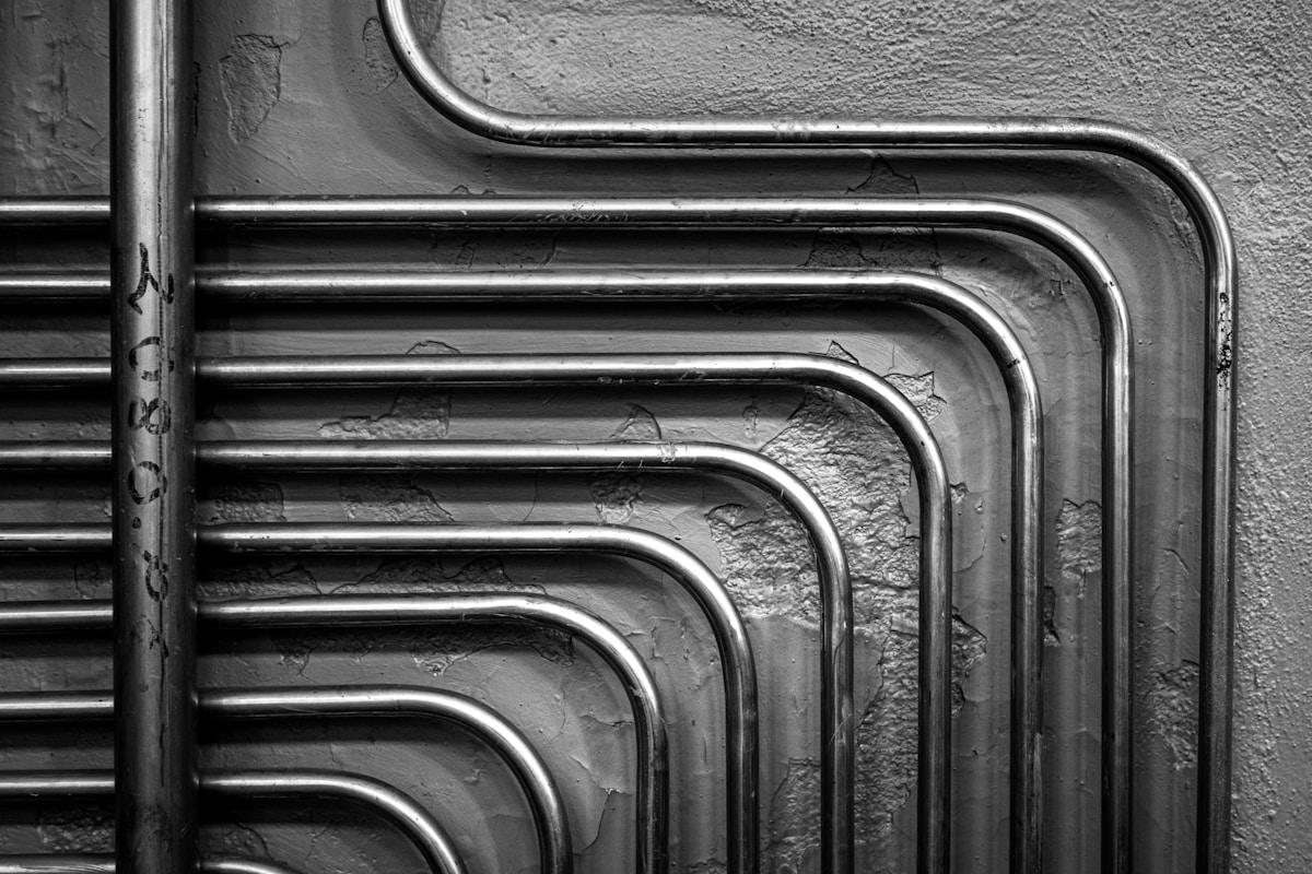 Tuyaux métalliques courbés et texturés sur un mur gris.