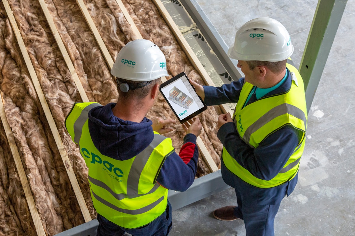 Deux ouvriers du bâtiment en tenue de sécurité examinent une tablette numérique sur un chantier.