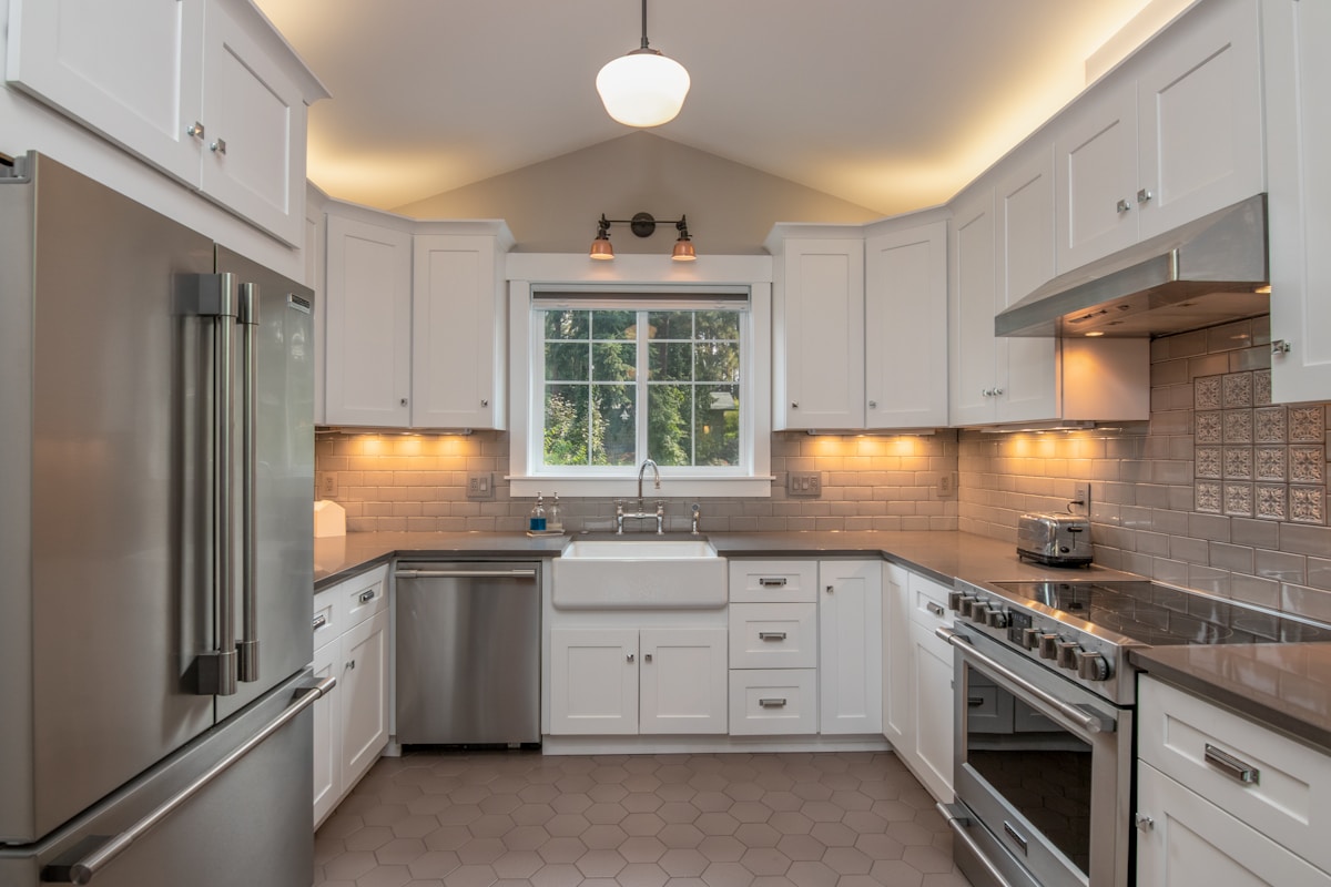 Cuisine moderne et lumineuse avec armoires blanches, électroménagers en acier inoxydable et carrelage hexagonal.