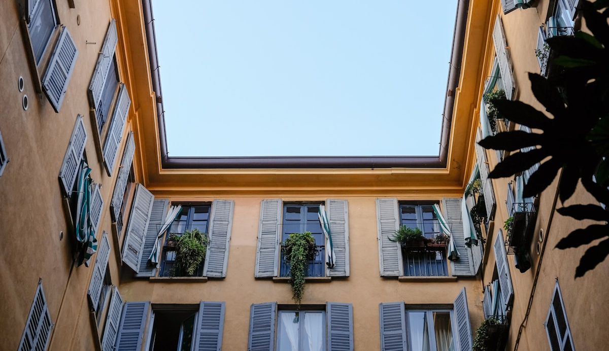 Fenêtres avec volets bleus, balcons fleuris, ciel bleu lumineux.