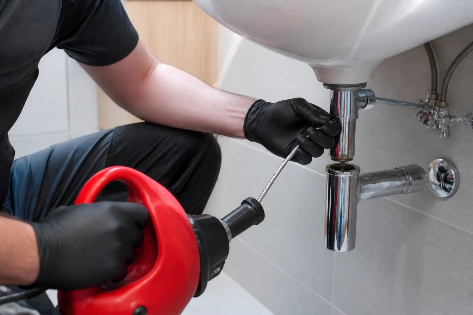 Plombier en gants noirs réparant un évier de salle de bain.