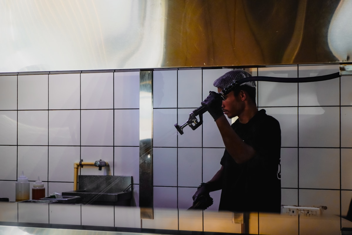 Homme en tenue noire tenant un microphone dans une cuisine.
