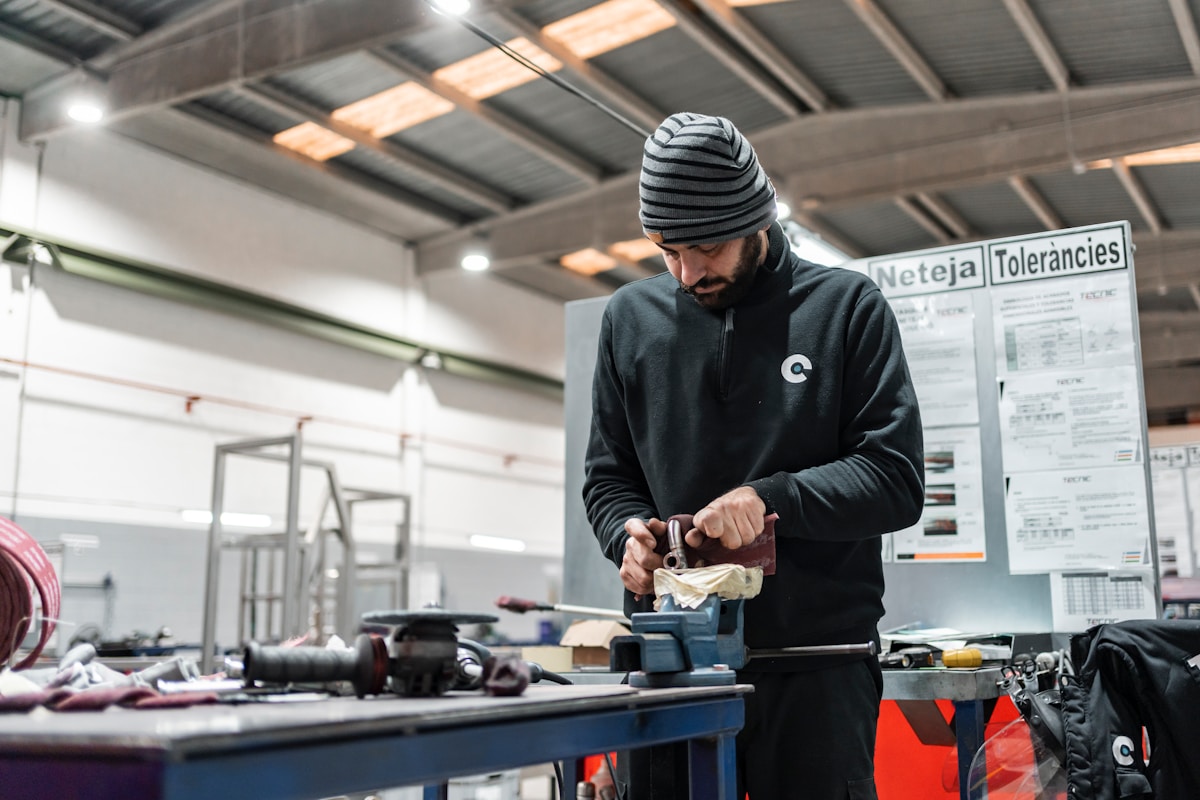Un homme barbu en tenue de travail utilise un outil dans un atelier.