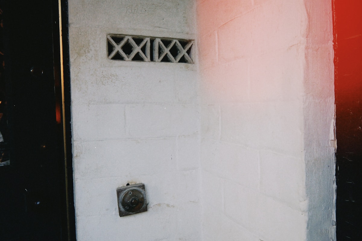 Mur blanc avec fenêtre grillagée et interphone.