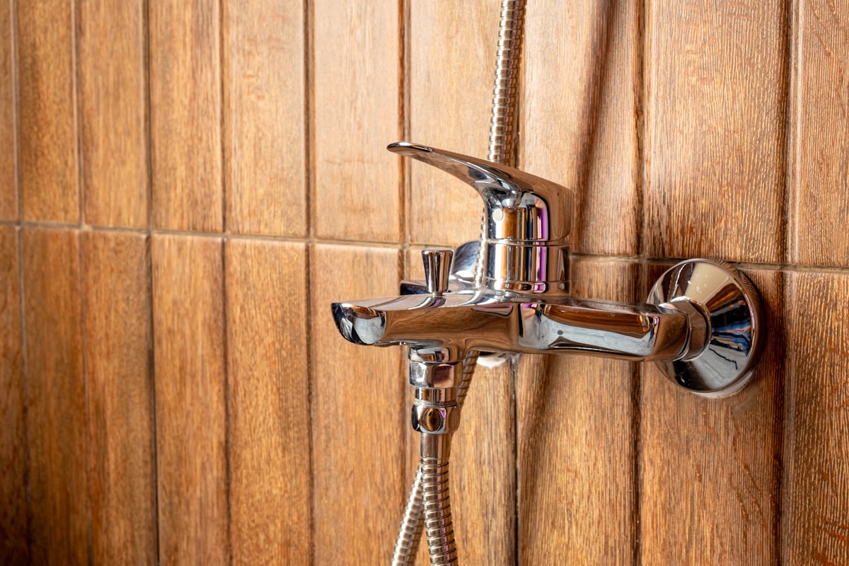 Robinet de douche chromé sur fond de panneaux de bois.