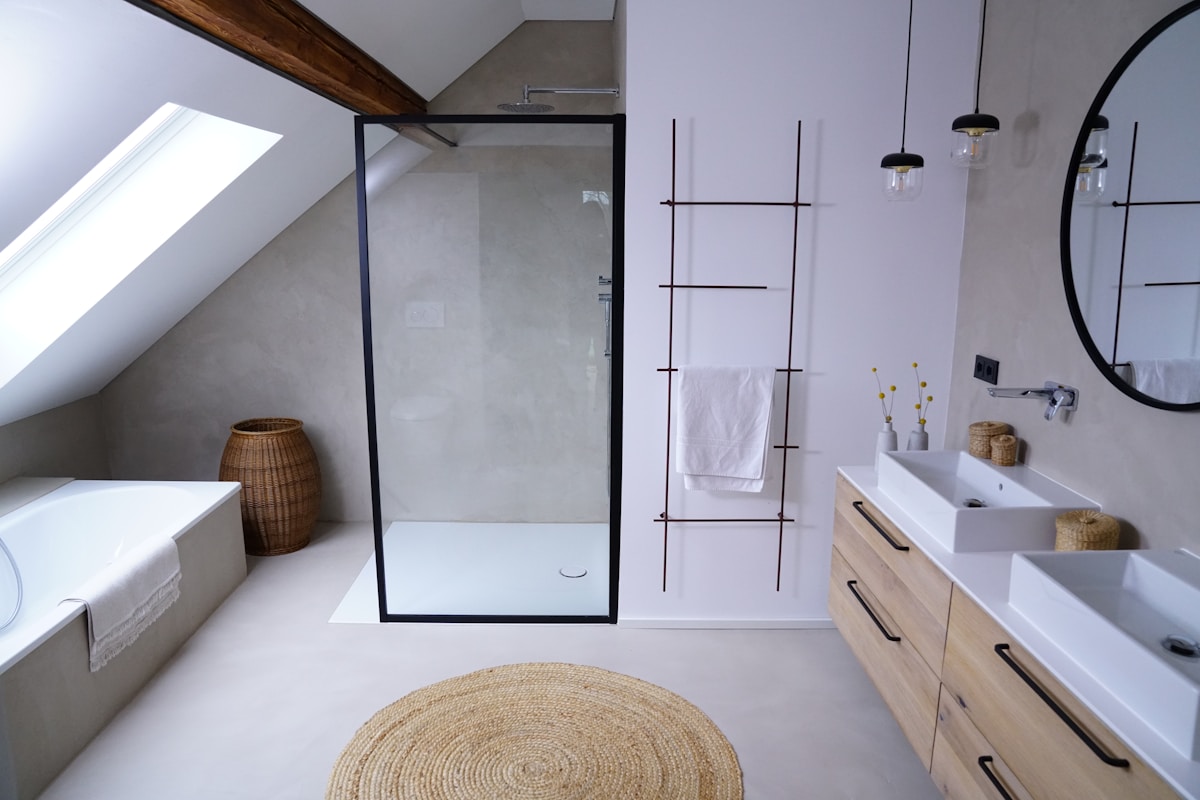 Salle de bain moderne avec douche en verre, meuble de rangement et accessoires naturels.