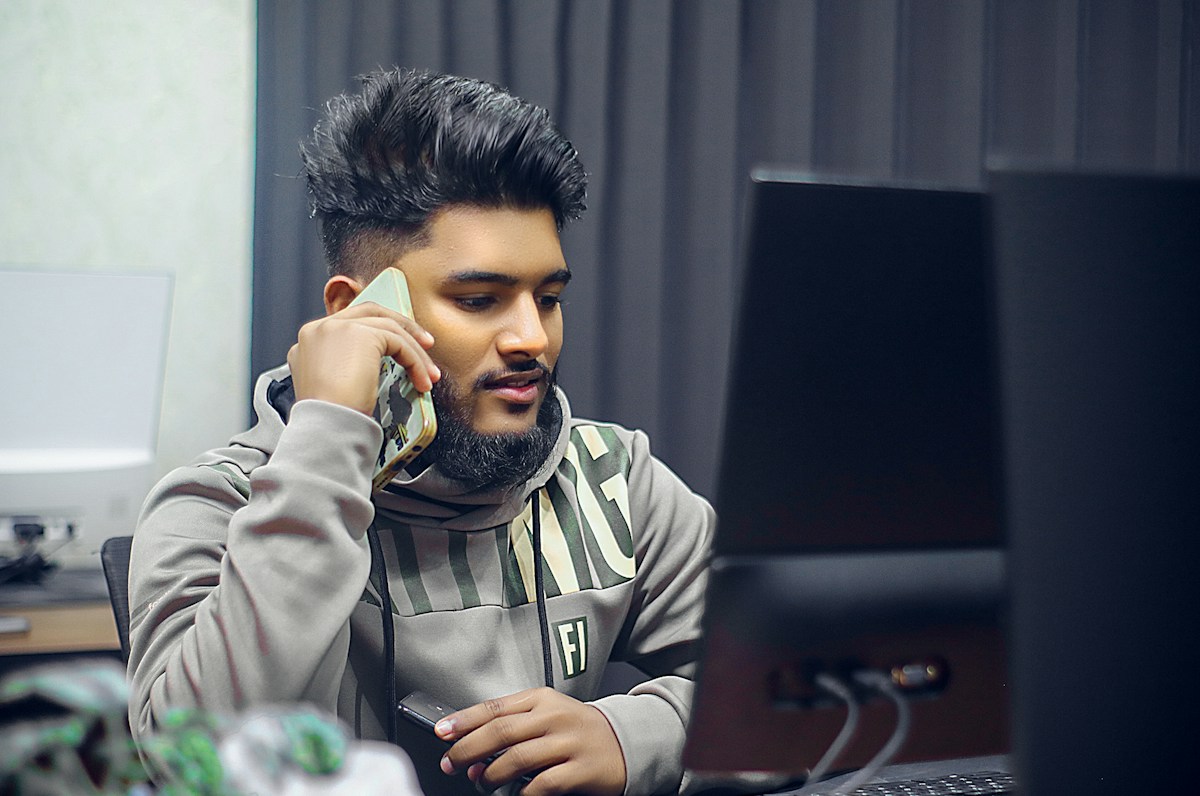 Homme barbu au téléphone devant un écran d’ordinateur.